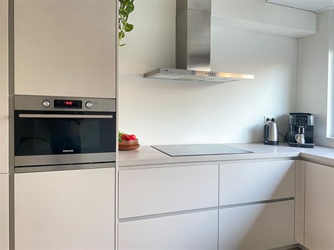 Witte keuken met inbouwoven, werkblad en afzuigkap.