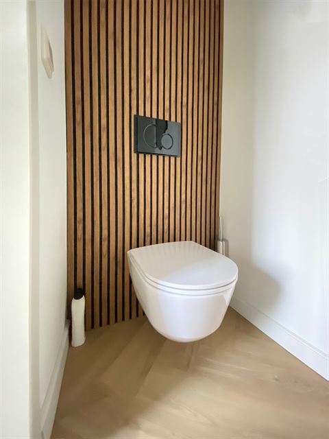 Toiletruimte met wandcloset en houten wandafwerking.