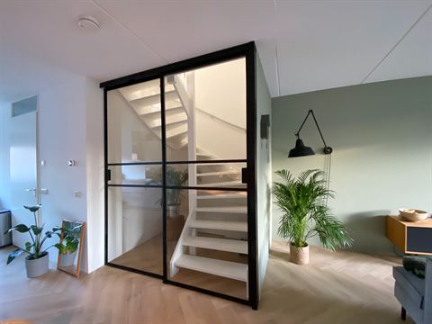 Trap achter de glazen wand met zwart frame, naast de woonkamer.