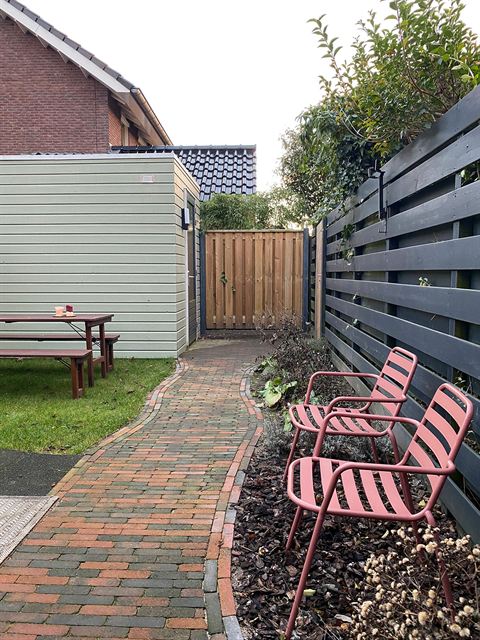 Achtertuin met terras, beplanting en berging aan het einde van de tuin.
