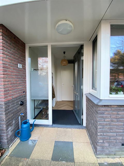 Overdekte entree met de geopende voordeur.