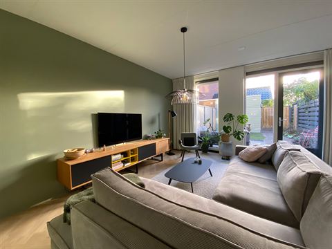 Overzicht van de woonkamer met bank, televisie en ramen aan de tuinzijde.