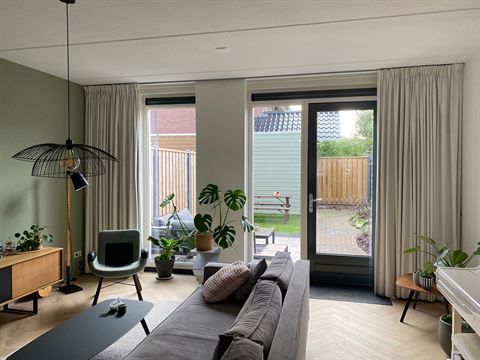 Woonkamer met piano, bank en zicht op de achtertuin.
